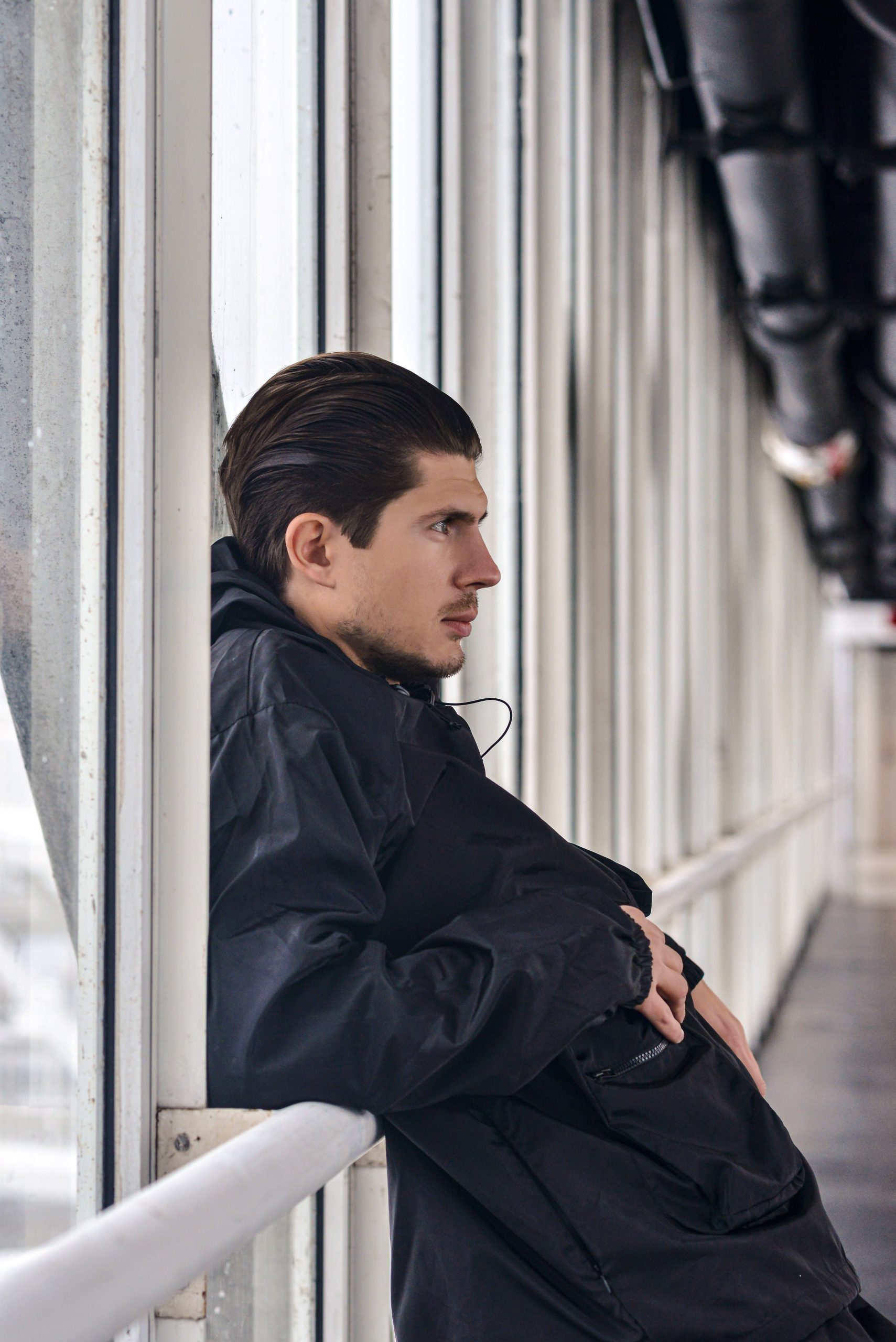 Man wearing a windbreaker pullover jacket in a futuristic/modern setting in grey lighting.
